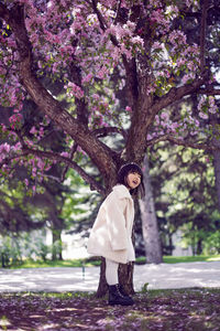 Korean girl in a white light fur coat and a headband stands in a garden with cherry blossoms