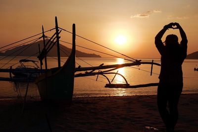 Silhouette man standing in sea against orange sky