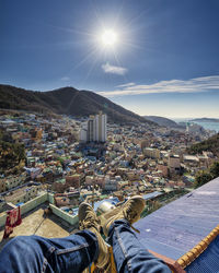 Low section of man sitting against cityscape during sunny day