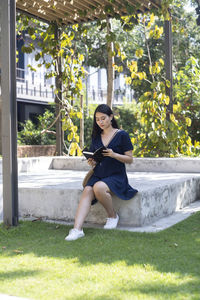 Portrait of young woman sitting on grass against plants