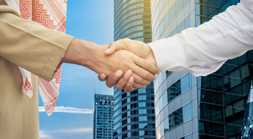 Cropped hands of business people giving handshake against buildings