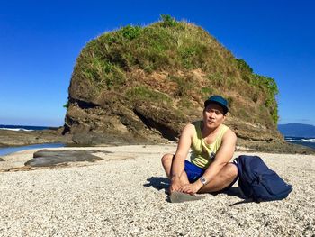 Young woman sitting on rock at beach against clear sky