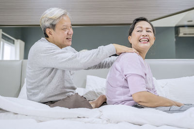 Smiling man massaging woman on bed at home