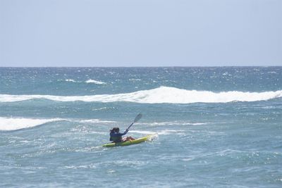 Woman kayaking in sea against clear sky