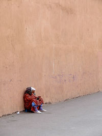 Homeless woman sitting by wall on street
