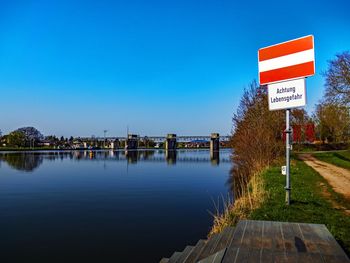 Information sign by lake against clear blue sky