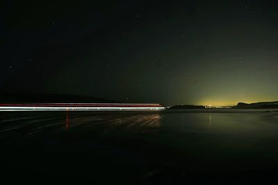 Light trails over lake against sky at night