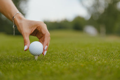 Woman's hand with a manicure puts a golf ball on a tee on a golf course