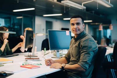 Portrait of confident businessman sitting at desk while female colleagues working in creative office