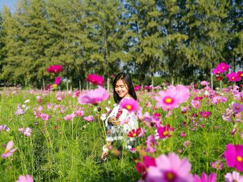 Smiling woman standing amidst cosmos field on sunny day