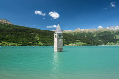 Old tower in river by mountains against sky