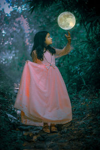 Digital composite image of girl standing by moon in mid-air at forest