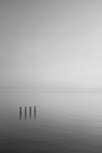 Wooden posts in sea against clear sky