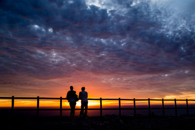 Silhouette men standing against dramatic sky during sunset