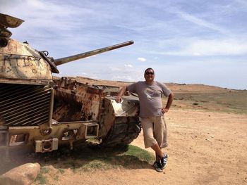 Man standing by abandoned military tank against sky