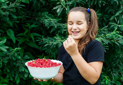 Girl holding raspberries in bowl against plants