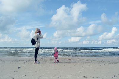 Mother and daughter at beach against sky