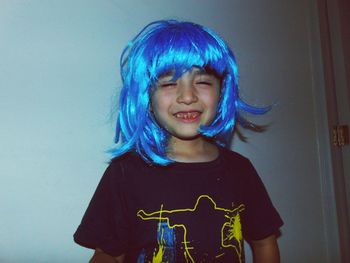 Smiling boy wearing wig while standing against wall