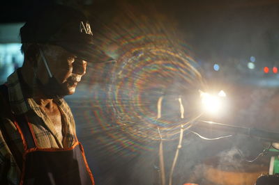 Side view of man looking at illuminated city at night