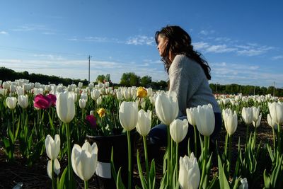 Rear view of woman standing by tulips against sky