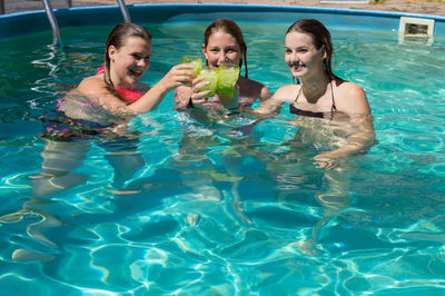 Happy female friends toasting drinks while enjoying in swimming pool