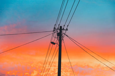 Low angle view of silhouette electricity pylons against sky during sunset