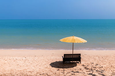 Empty bench and umbrella on beach against clear sky