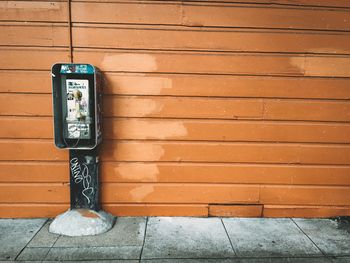 Pay phone on footpath against brown wall