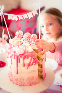 Girl reaching for candy on birthday cake at party