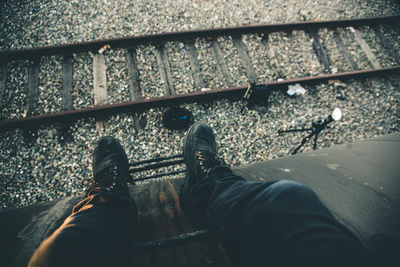 Cropped image of man sitting on cargo container by railroad track