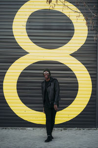 Young black man on city street in front of a black wall with the number eight in yellow