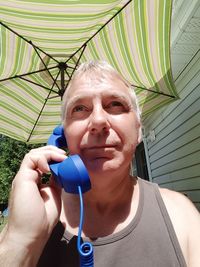 Mature man talking on landline phone while standing against parasol
