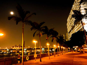 Illuminated buildings by street against sky at night