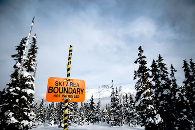 Low angle view of warning sign against sky during winter