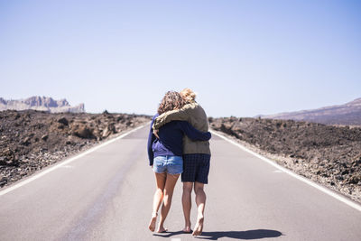 Rear view of woman walking on road against clear sky
