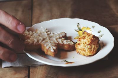 Cropped hand holding gingerbread cookie in plate on table