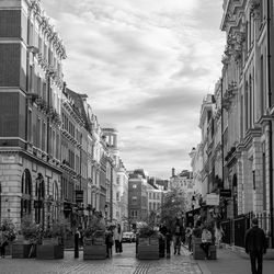 People walking on street amidst buildings in city against sky