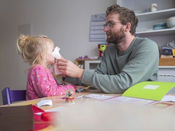 Playful father holding paper on daughter's while sitting at table