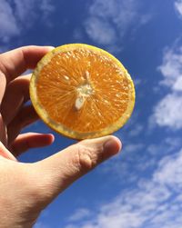 Close-up of hand holding apple against sky