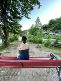 Rear view of woman sitting on sidewalk against sky