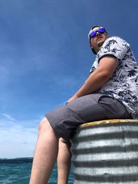 Midsection of woman sitting by sea against sky