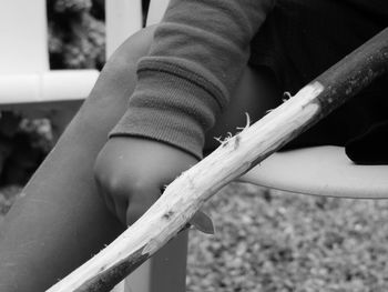 Midsection of person holding wood while sitting outdoors