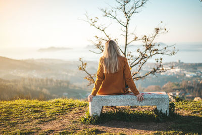 Rear view of woman sitting on bench against sky