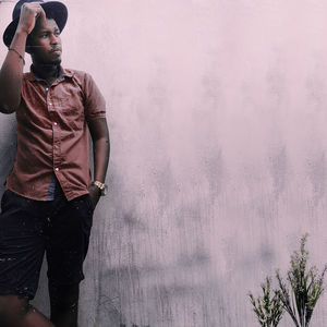 Thoughtful young man wearing hat while standing against wall