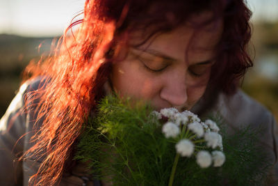 Close-up of redhead woman with eyes closed smelling white flowers