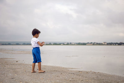 Rear boy child in blue shorts walks by the lake in summer