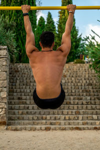 Rear view of shirtless man looking at stone wall