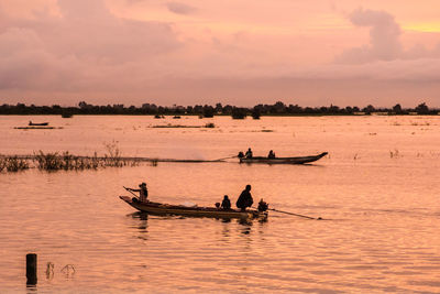 Silhouette men in boat on lake against sky