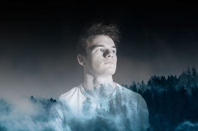 Double exposure image of young man and trees against sky at foggy night
