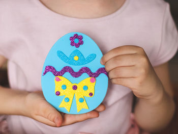 The hands of a little caucasian girl shows the final result of a blue easter felt egg with sticker
